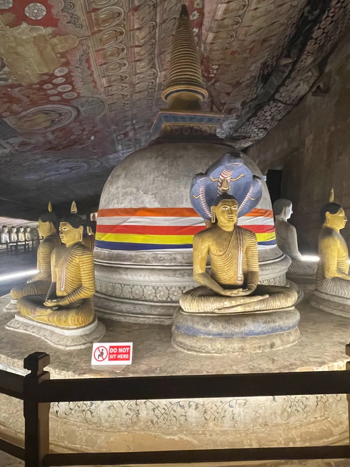 A small stupa surrounded by seated Buddha statues inside a painted cave at Dambulla