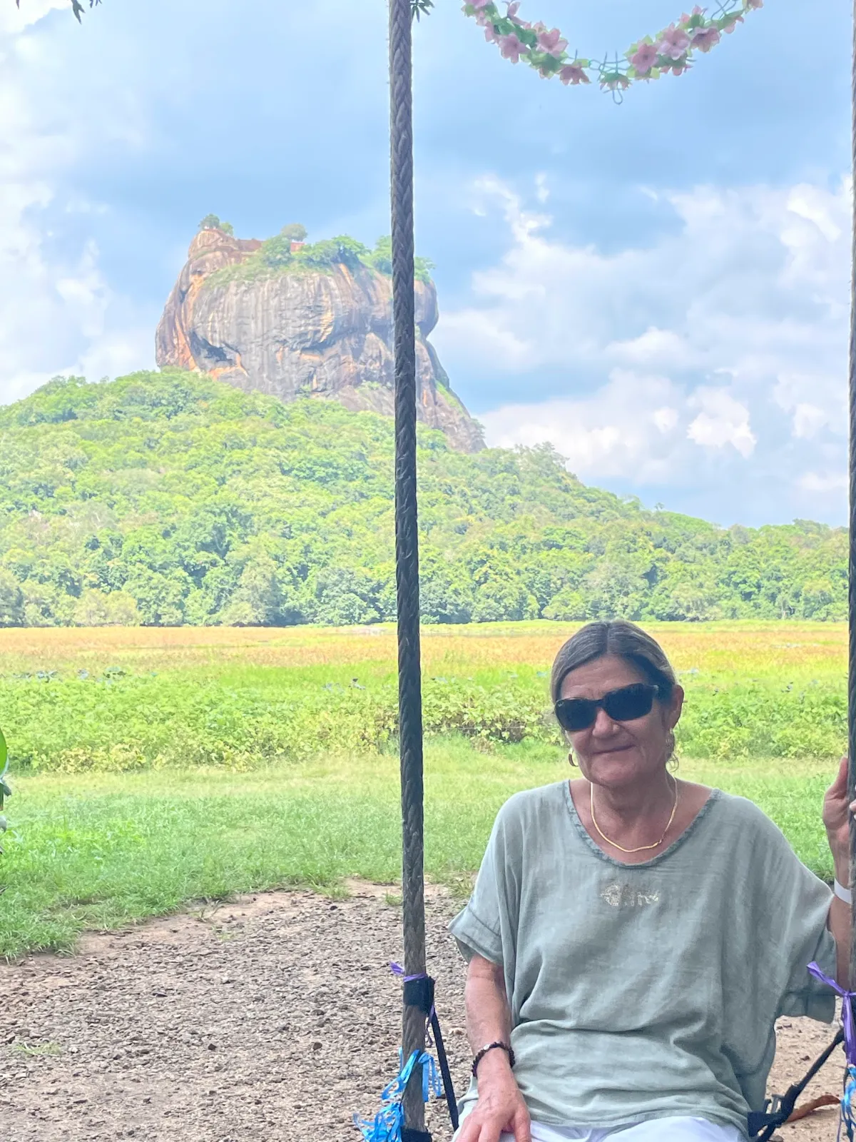 A smiling traveller on a swing with Sigiriya rock behind her